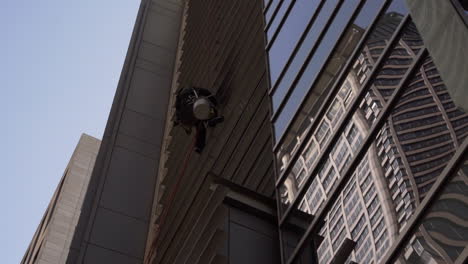 Un-Limpiador-De-Ventanas-Lanza-Agua-Mientras-Trabaja-En-Lo-Alto-De-Un-Edificio.