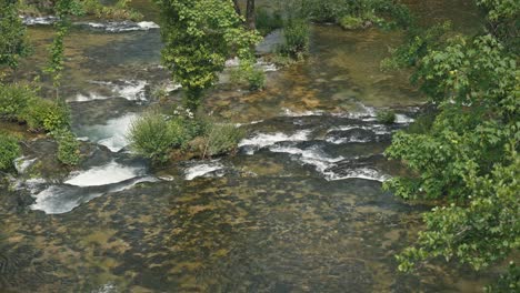 Shallow-waters-of-the-Slunjčica-River-with-rocks-and-lush-greenery-in-Rastoke,-Croatia