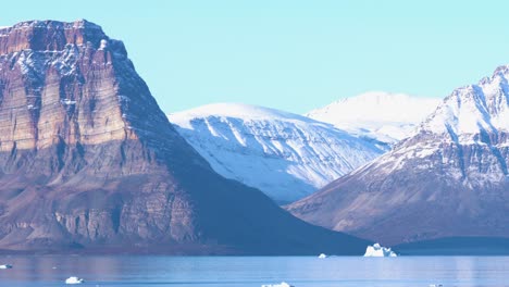 Northeast-National-Park-of-Greenland,-Steep-Hills-and-Snow-Capped-Peaks-Above-Fjord-and-Cold-Sea-on-Sunny-Day