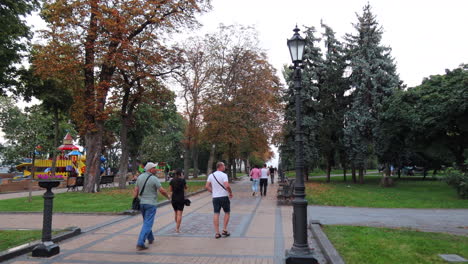 People-walking-at-a-beautiful-nature-park-with-a-kids-playground-in-Kyiv-city-center-Ukraine,-green-grass-and-trees,-4K-shot