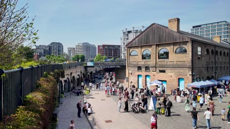 Coal-Drops-Yard-in-Kings-Cross,-London,-with-people-strolling-on-a-sunny-day,-showcasing-the-concept-of-urban-leisure-and-modern-architecture