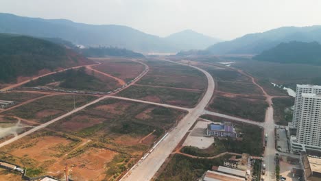 Aerial-view-of-roads-winding-through-the-Boten-Special-Economic-Zone-in-Laos-near-the-China-border,-featuring-newly-built-buildings-with-a-scenic-landscape-backdrop,-Belt-and-Road-Initiative