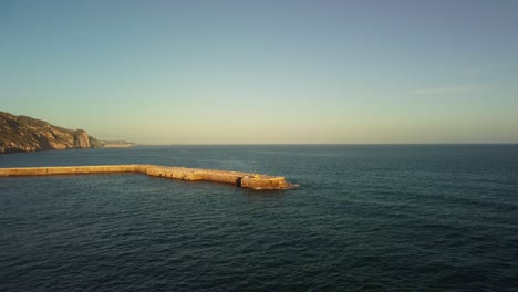 Costa-Garraf-Al-Atardecer-Con-Una-Fábrica-De-Cemento-En-La-Distancia,-Vista-Aérea