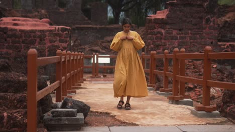 Woman-in-yellow-dress-walks-on-bridge-in-ancient-ruins-on-a-cloudy-day