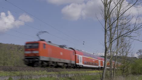 Roter-Zug-Der-Deutschen-Bahn-Rast-Mit-Bewegungsunschärfe-An-Der-Landschaft-Vorbei,-Sonniger-Tag