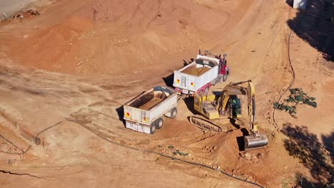 Camión-Y-Remolque-Estacionados-Junto-A-Un-Montón-De-Tierra-Mientras-Una-Excavadora-De-Orugas-Carga-Tierra