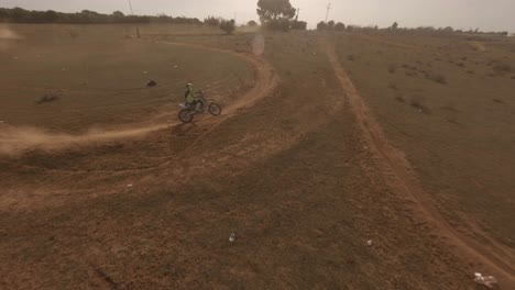 FPV-camera-follows-moto-racer-on-dusty-sand-track-on-golden-sunny-day