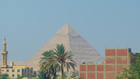 Great-Pyramid-of-Giza-beyond-the-city-in-desert-haze,-view-from-car