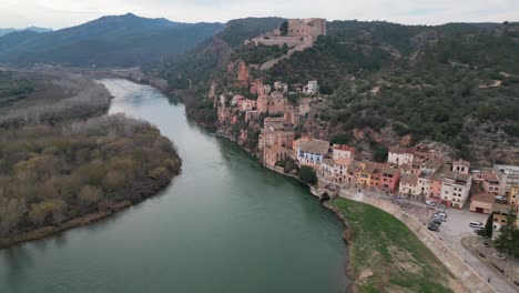 Historic-Miravet-town-and-castle-on-a-hilltop-by-a-winding-river-in-Tarragona-Spain,-aerial-view