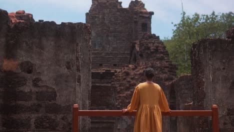 A-monk-in-an-orange-robe-explores-ancient-ruins-under-a-bright-blue-sky