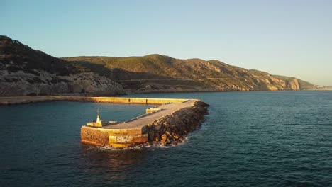 A-coastal-pier-at-costa-garraf-with-scenic-mountains-in-the-background,-aerial-view