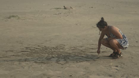 Frau-Zeichnet-Ein-Muster-In-Den-Sand-Am-Strand