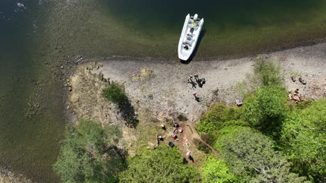Tourist-family-enjoy-lunch-break-on-a-hidden-island-during-Fjord-safari,-top-down-aerial
