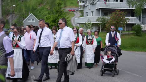 Personas-Vestidas-Con-Trajes-Nacionales-Marchan-En-Una-Ciudad-Rural,-Celebrando-El-Día-De-La-Constitución-De-Noruega.