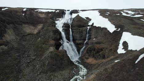 Aerial-reveal-shot-of-the-Rjukandafoss-waterfall-in-East-Iceland,-featuring-its-two-tiered-cascade-and-lush-surroundings
