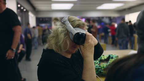 Middle-aged-Caucasian-woman-tries-on-a-virtual-reality-headset-inside-electronics-store