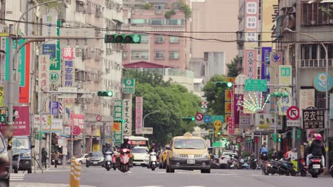 Street-view-with-signs,-traffic-lights,-and-scooters-passing-by-in-Taipei-City,-Taiwan