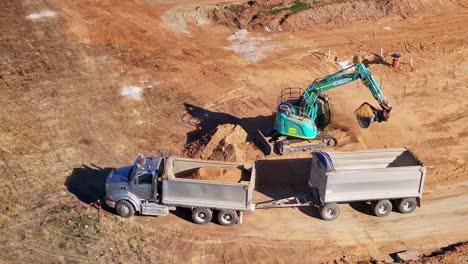 Yarrawonga,-Victoria,-Australien-–-29.-Mai-2024:-LKW-Und-Anhänger-Bringen-Sich-In-Position,-Damit-Ein-Raupenbagger-Erde-Von-Einem-Erdhaufen-Laden-Kann