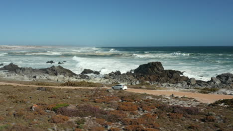 Weißer-Volkswagen-Polo-TSI-Fährt-Auf-Einer-Unbefestigten-Straße-Entlang-Der-Küste-Des-West-Coast-National-Park,-Südafrika-–-Tracking-Drohnenaufnahme