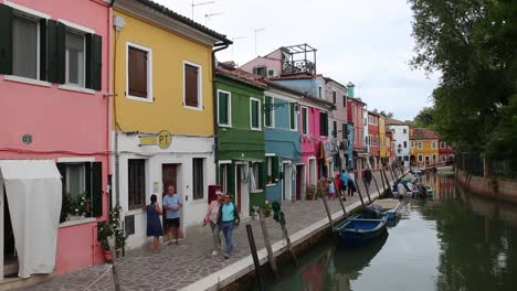 People-walk-by-colourful-vibrant-houses-along-canal,-Burano-island-Venice,-Italy