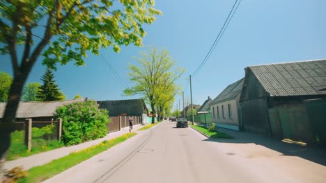 Pov-on-Baltic-village-street-in-countryside-with-road,-house,-car,-pedestrian-during-spring