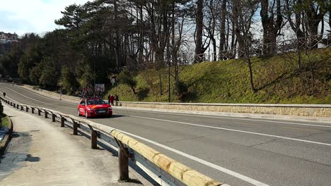 El-Coche-Del-Equipo-De-Carreras-De-Ciclismo-Rojo-Pasa-Por-La-Carretera,-Tiro-En-Cámara-Lenta