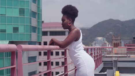 A-black-girl-in-a-white-dress-stands-on-a-rooftop,-looking-at-the-city-below