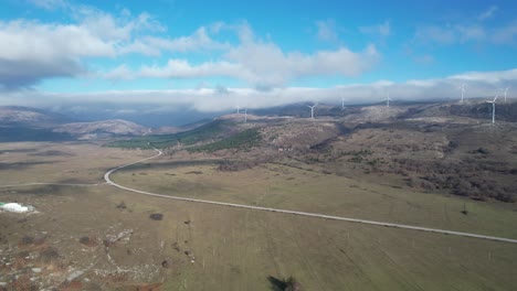 Beautiful-aerial-shot-of-Croatian-landscape-with-wind-turbines-generating-renewable-energy-in-the-background-and-an-empty-road,-in-the-region-of-Lika-in-Croatia,-Europe