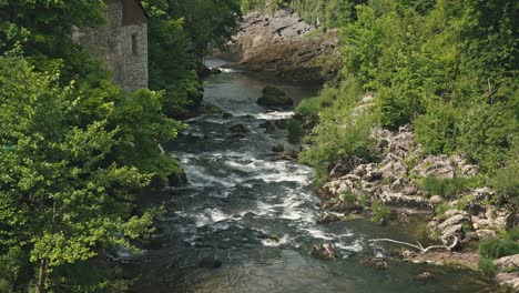 Scenic-river-view-with-a-historic-stone-building-and-lush-greenery-in-Rastoke,-Croatia