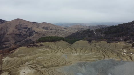 Aerial-perspective-of-the-volcanic-landscape-of-the-mountains-of-Romania-with-its-mud-volcanoes,-dry-land-with-cracks,-with-some-isolated-houses-and-villages