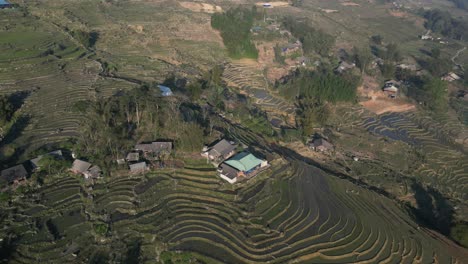 Aerial-drone-shot-flying-over-bright-green-rice-terraces-and-highland-villages-in-the-mountains-of-Sapa,-Vietnam