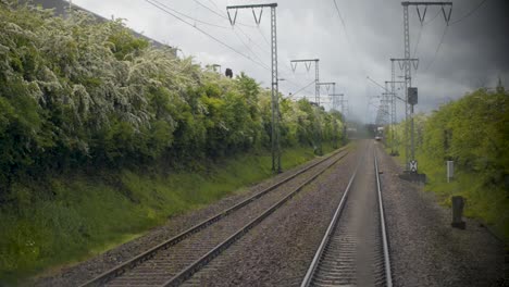 POV-shot-of-train-tracks-leading-forward-with-approaching-train,-cloudy-sky