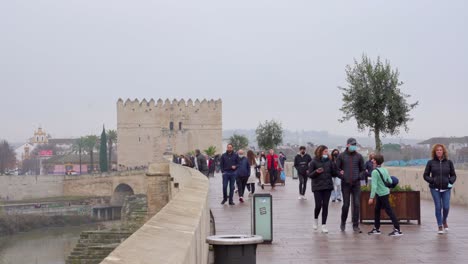 People-walking-on-Roman-Bridge-of-Cordoba-of-Andalucia,-Spain-on-an-overcast-day-during-Covid-19-Pandemic