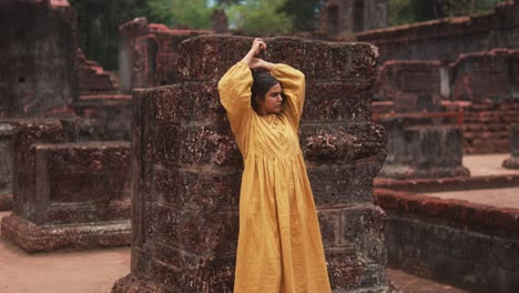 Mujer-Con-Un-Vestido-Amarillo-Posando-Contra-Antiguas-Ruinas-De-Piedra.