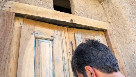 Un-Hombre-Está-Cerrando-Una-Puerta-De-Madera-Tradicional-En-Ruinas-De-Un-Antiguo-Edificio-Histórico-Antigua-Casa-En-El-Desierto-Casa-Oasis-Marruecos-Paisaje-Cultural-Vista-Interior-De-La-Casa-De-La-Gente-Local-Pobreza-Irán-Oriente-Medio