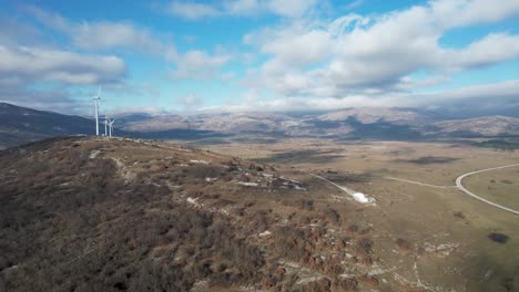 Beautiful-aerial-shot-of-Croatian-landscape-with-wind-turbines-generating-renewable-energy-in-the-background-and-an-empty-road,-in-the-region-of-Lika-in-Croatia,-Europe