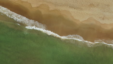 Slow-descending-shot-overhead-waves-crashing-on-a-golden-beach-in-Norway