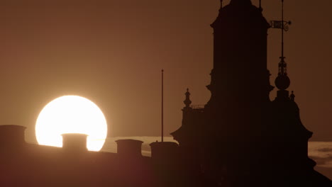 Sun-rising-in-golden-sky-over-Riddarholmen-Stockholm-skyline,-telephoto