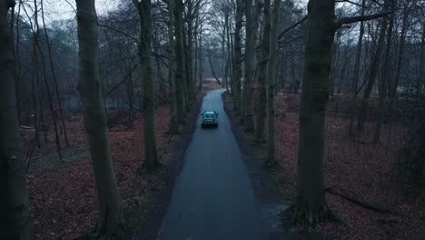 Aerial-view-of-a-modern-green-car-driving-on-a-country-road-surrounded-by-a-forest