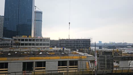 Timelapse-shot-panning-from-the-left-to-the-right,-showing-a-building-under-construction,-as-masons-and-other-builders-are-busy-working-using-cranes-and-other-heavy-equipment,-near-Danube-in-Austria