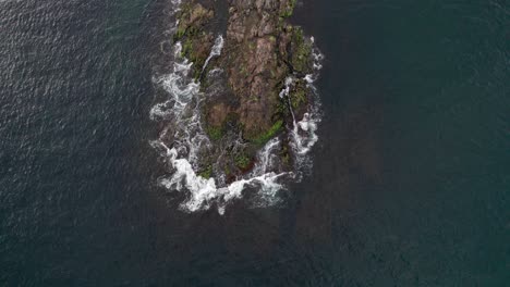 Birds-eye-view-crossing-a-rock-in-the-white-foaming-ocean-waters-of-Newport,-Rhode-Island