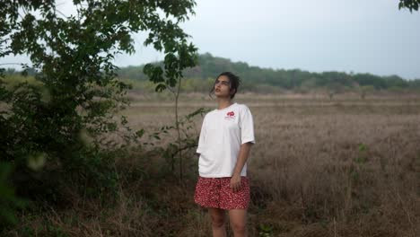 Young-woman-stands-in-a-field-with-trees,-looking-determined