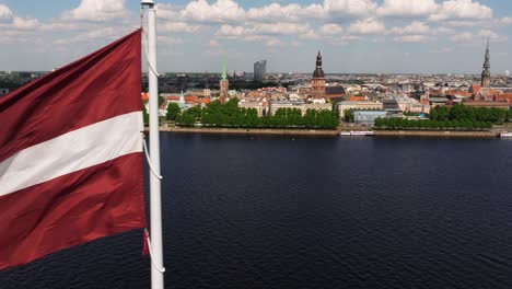 Close-Up-Aerial-View-of-Latvian-Flag-Waving-in-Wind---Riga,-Latvia-in-Background