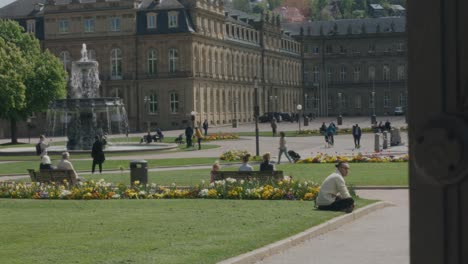 Man-sitting-on-lawn-in-thought-in-front-of-large-statue-of-Stuttgart-Parliament-building-at-noon,-Germany,-Europe