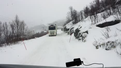 POV-shot-of-2-long-haul-cargo-trucks-cautiously-approaching,-as-they-struggle-to-pass-on-a-tight-narrow-mountain-pass,-the-roads-extremely-dangerous-covered-in-snow-and-ice-from-a-blizzard,-Norway