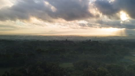 Silhouetted-Borobudur-temple-in-mystic-Indonesia-landscape,-dramatic-sunbeams-dancing-in-early-morning-mist