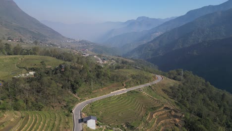 Aerial-drone-shot-of-road-driving-through-bright-green-rice-terraces-in-the-mountains-of-Sapa,-Vietnam