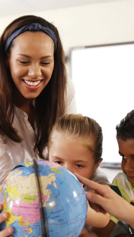 Teacher-assisting-school-kids-in-reading-globe-in-classroom