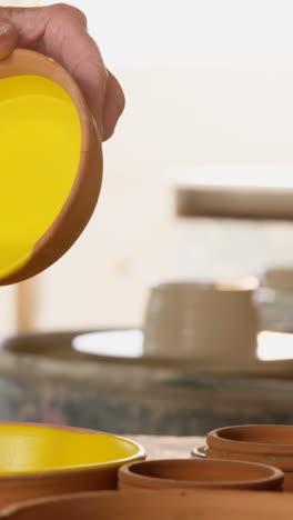 Mid-section-of-female-potter-pouring-paint-into-bowl