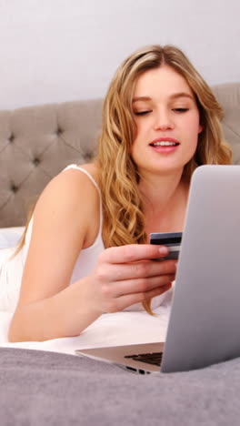 Woman-doing-online-shopping-with-her-laptop-on-bed